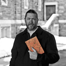 Poet Monty Milne holding his poetry book The Orange Book